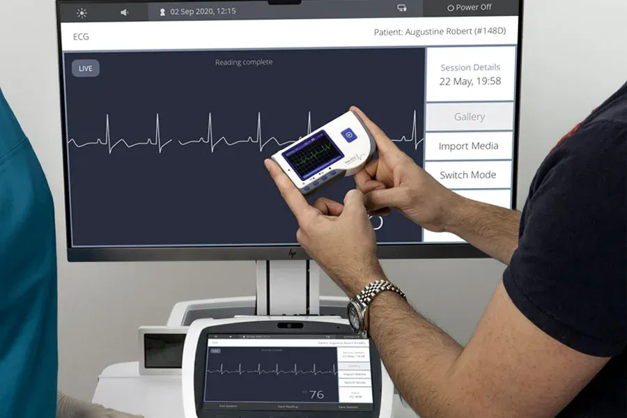 Healthcare professional holding a handheld ECG device beside a heart rhythm monitor
