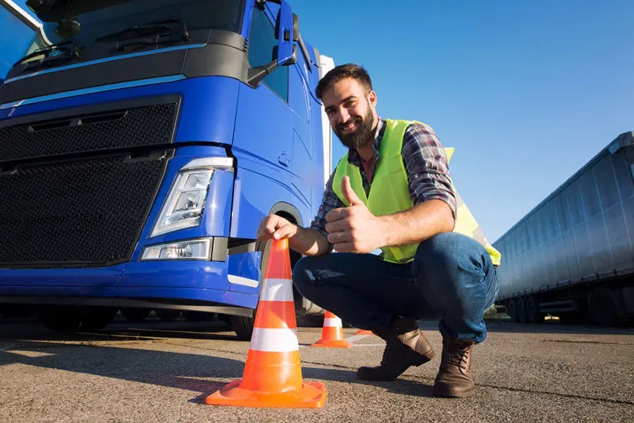 Man in a high-visibility vest giving a thumbs up beside a truck tyre