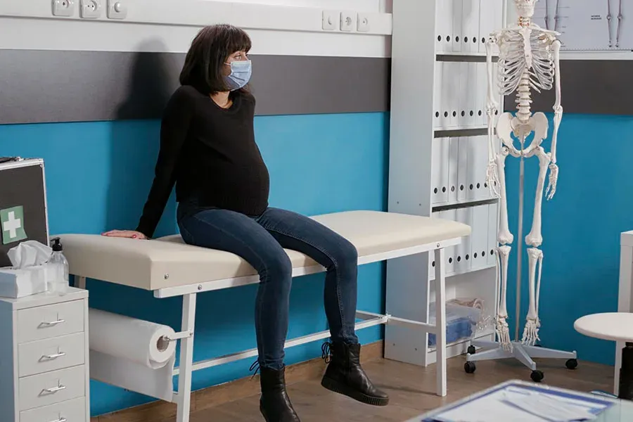 Pregnant woman seated on an examination table beside an ultrasound machine